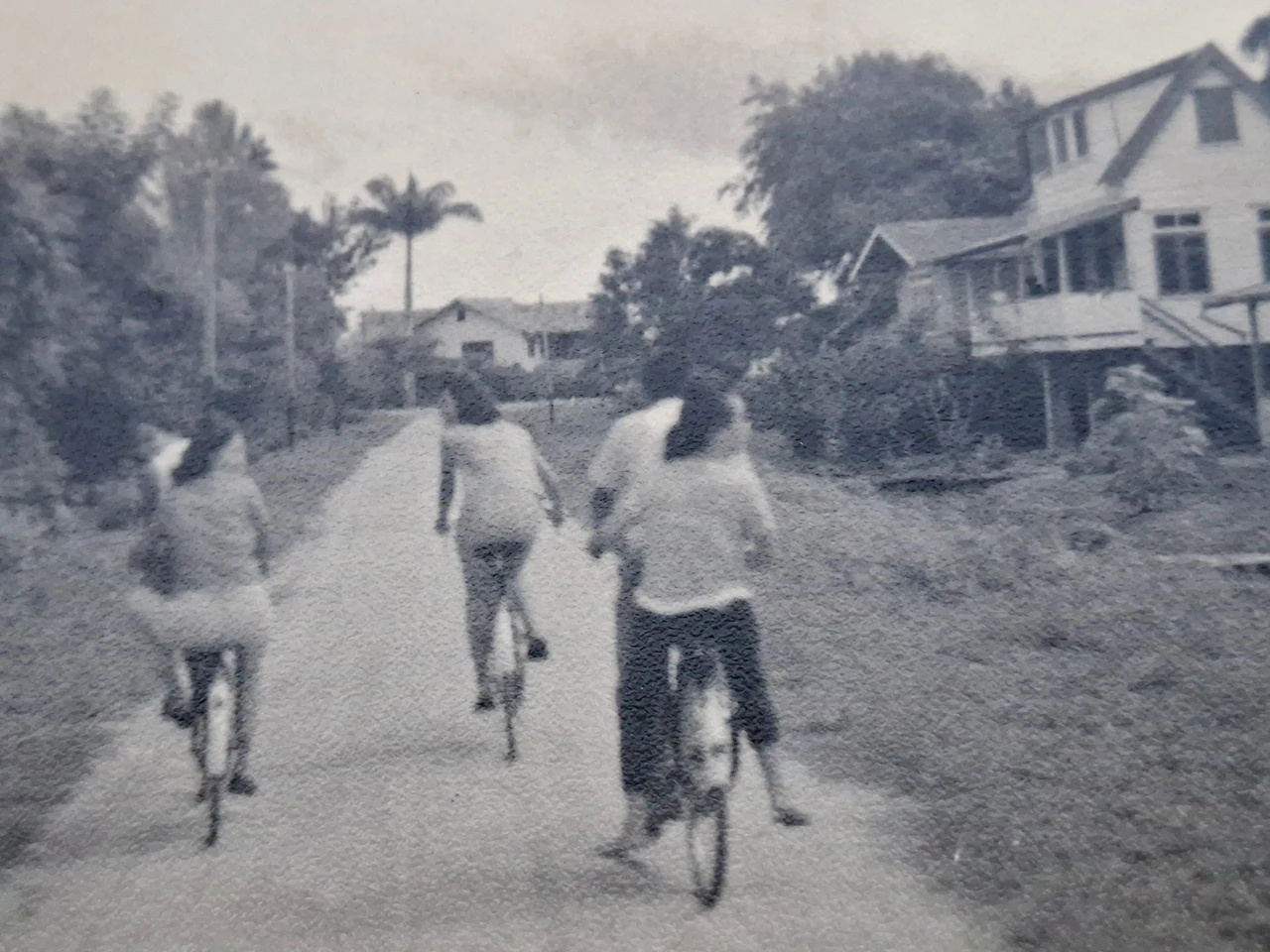 Historische zwart-witfoto van vier mensen op fietsen op een onverharde weg.