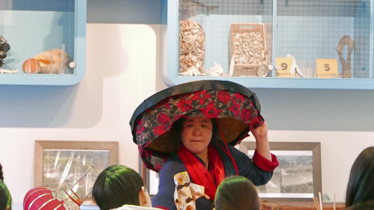 Vertelvoorstelling voor publiek, met een vrouw in een bloemrijke hoed.